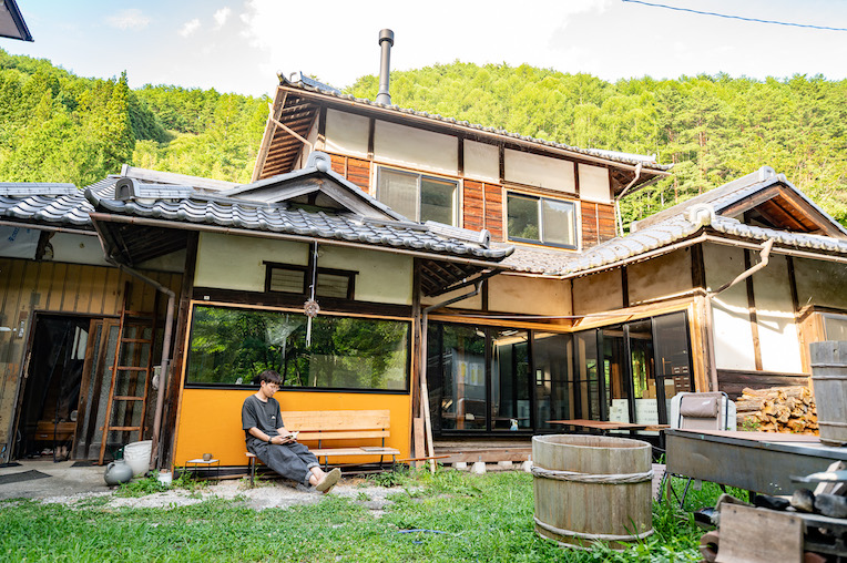 緑の山を背にした、大木さんが借りている母屋の外観。縁側のベンチに人が座っている